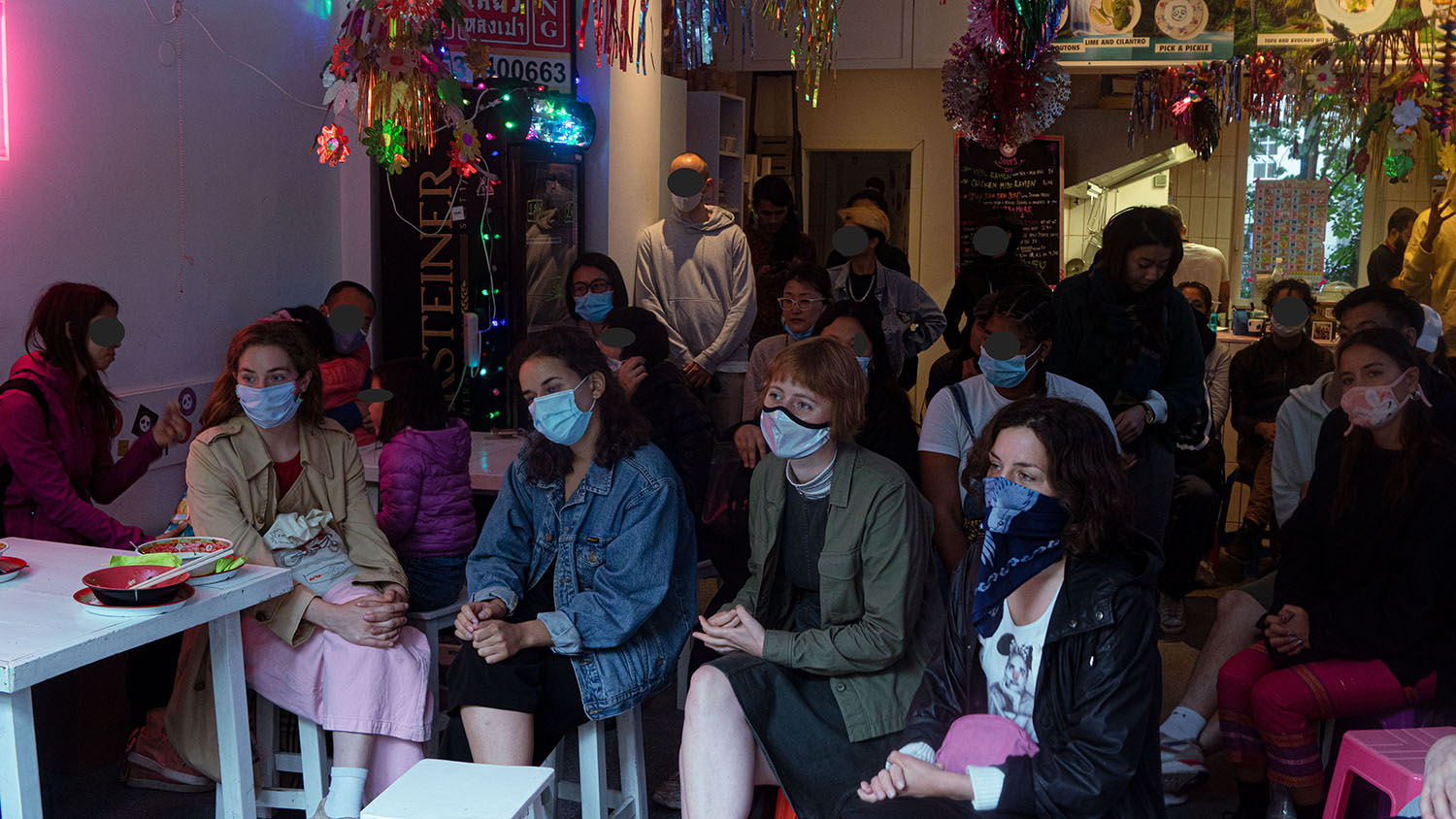 An audience, some people sitting on stools, some standing. Everyone is wearing a mask. The photo was taken during the #Mygration Event on 20.06.2020.