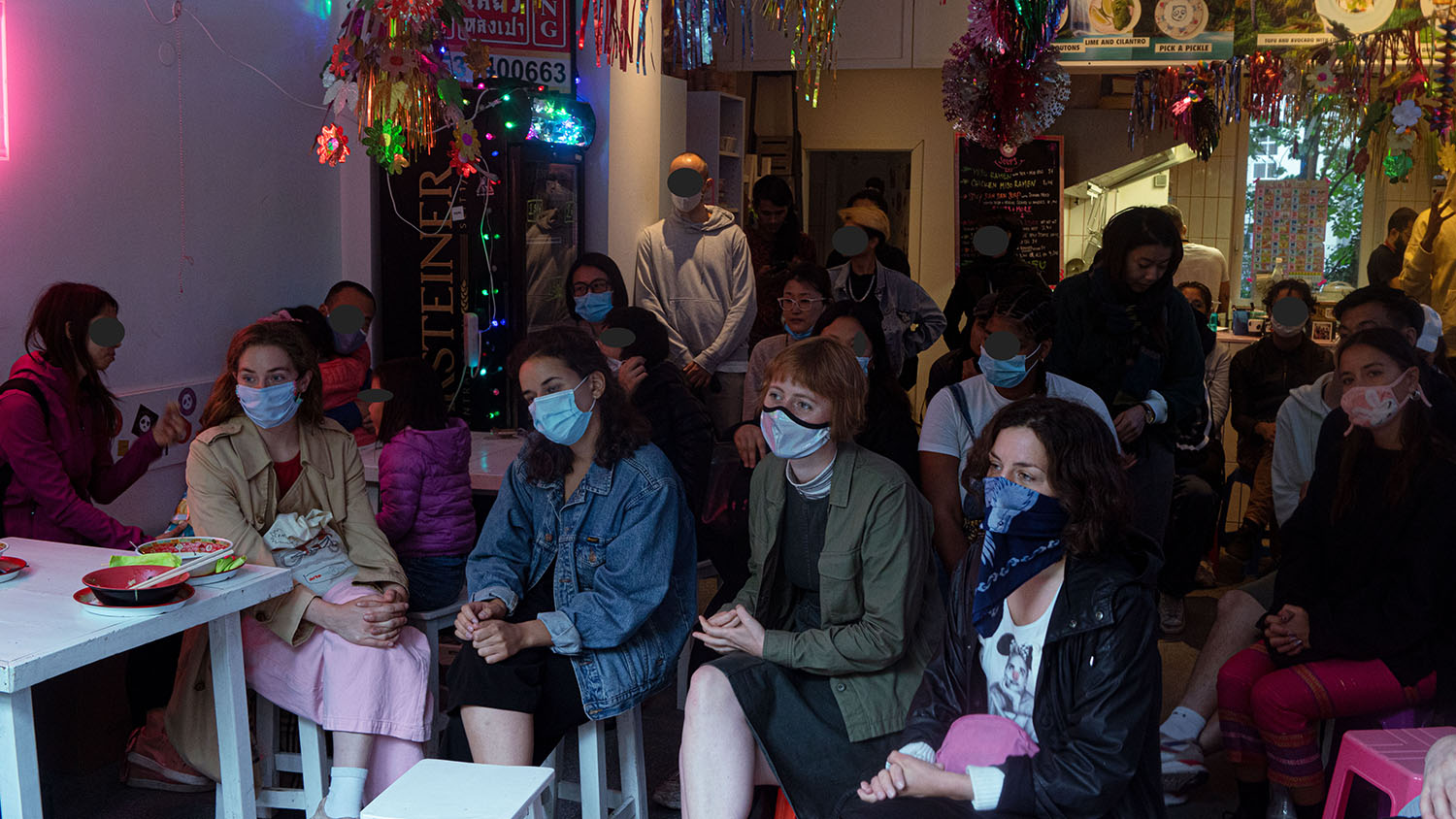 Ein Publikum, teils sitzen die Menschen auf Hockern, teils stehen sie. Alle tragen eine Maske. Das Foto entstand während des #Mygration Events vom 20.06.2020.